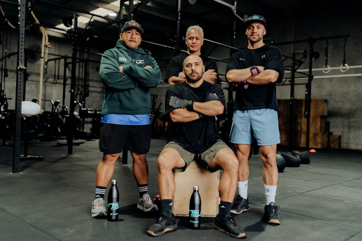 A crew of four tāne standing together at the gym with Wai July drink bottles