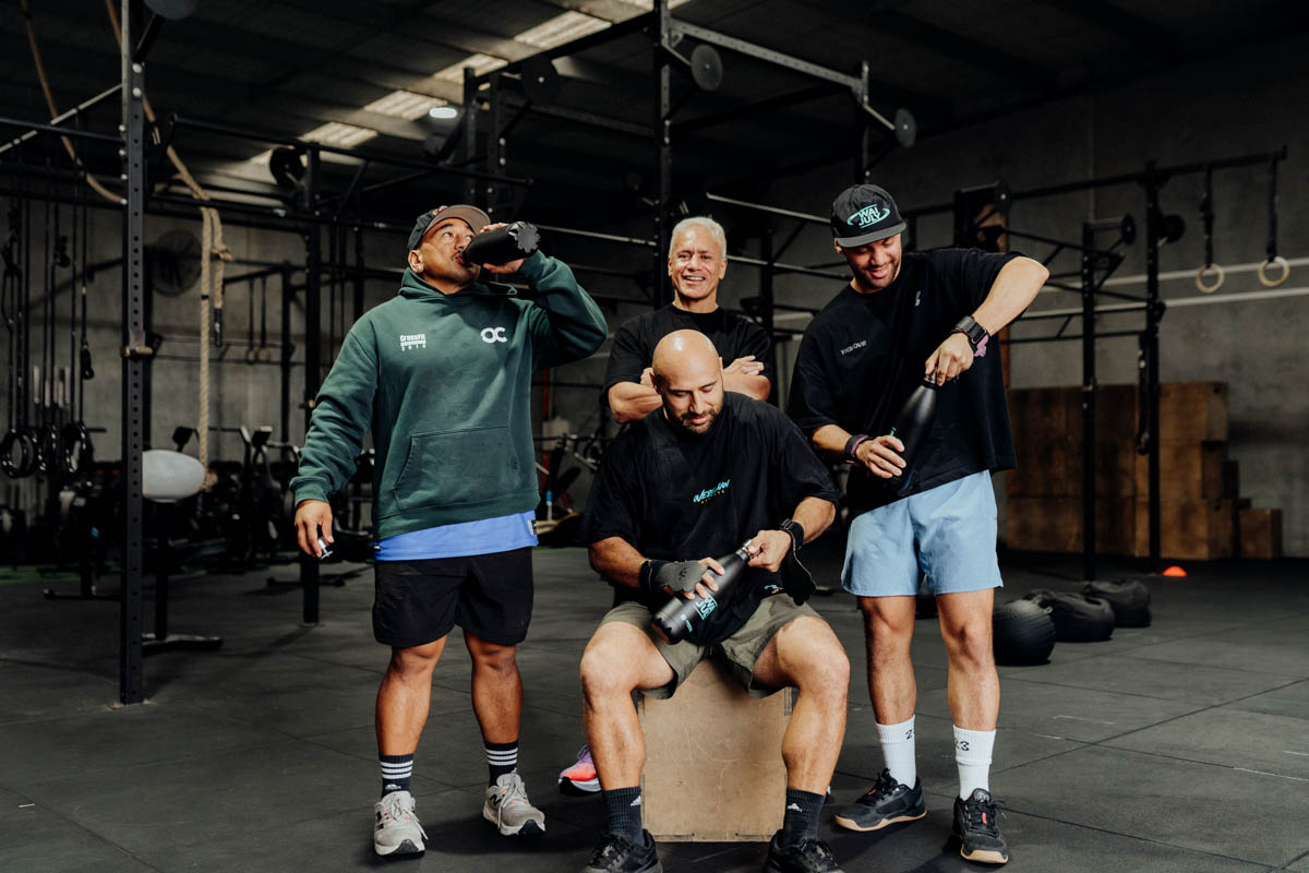 Four tāne laughing together at the gym, drinking from Wai July water bottles