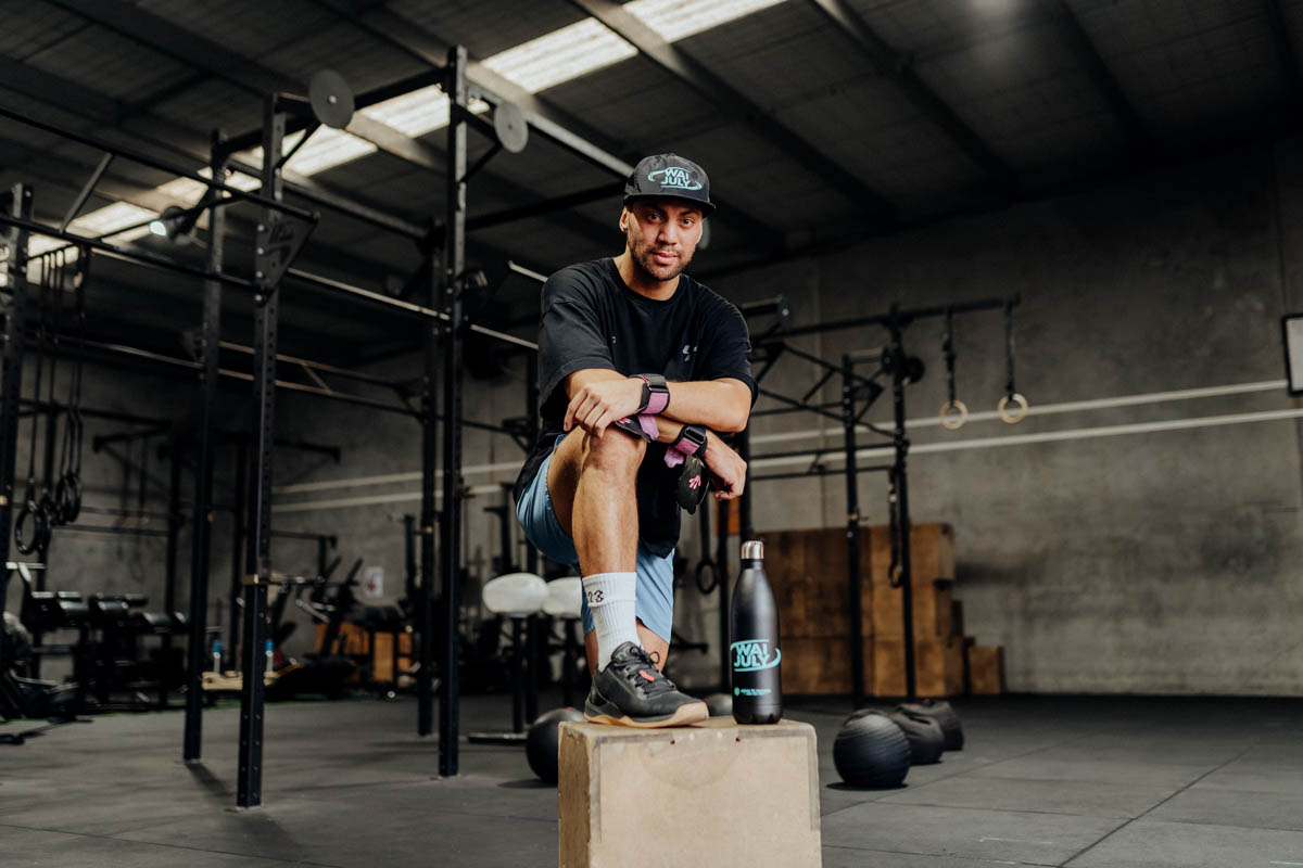A tāne taking a quiet moment on a gym box, Wai July cap and drink bottle beside him